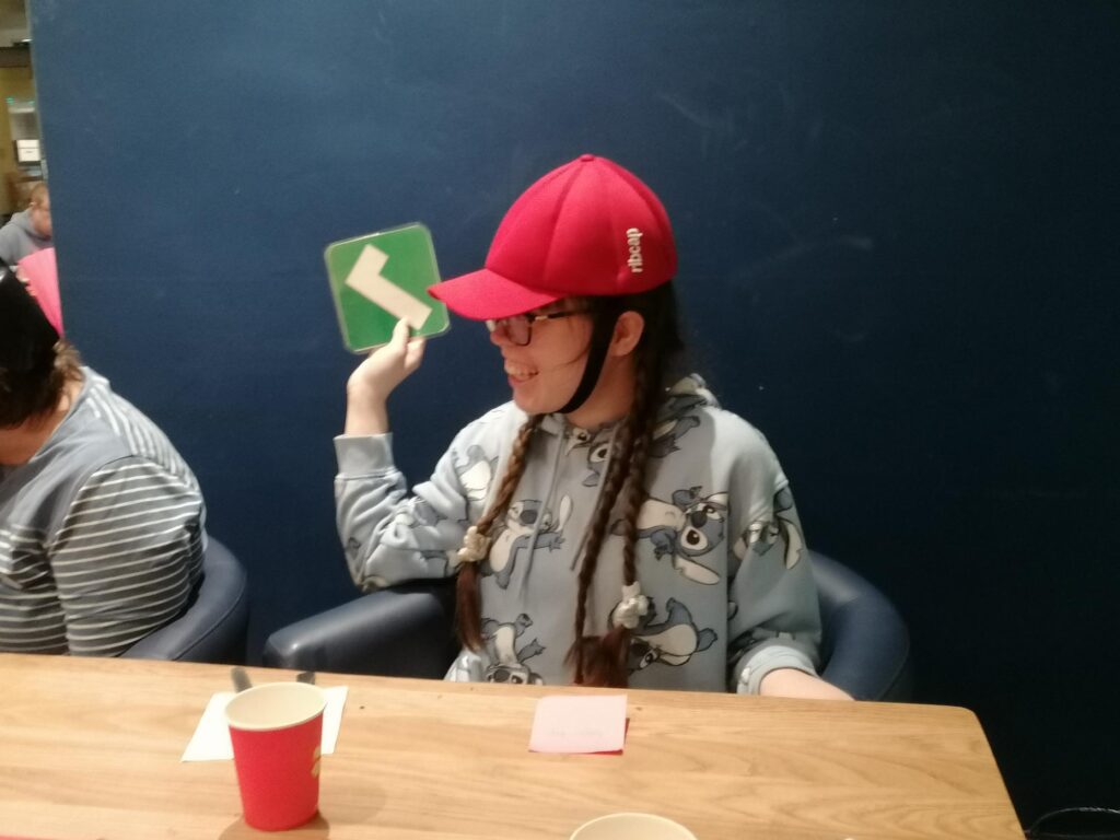 A woman in a red epilepsy helmet is smiling and holding up a tick symbol.