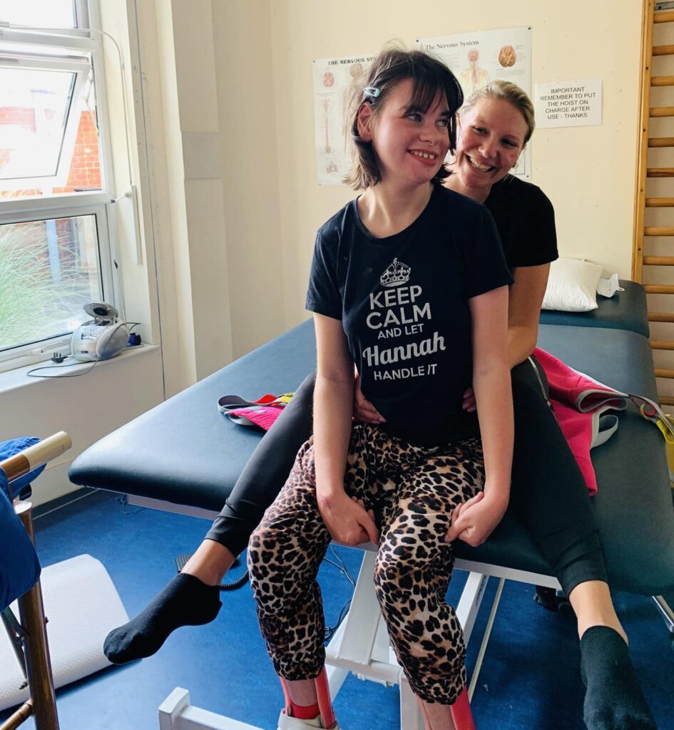 A young teenager sits on a physio bench with a woman sat beside her smiling.