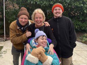 A man and woman smile next to a young man and in front of them is a young woman in wheelchair. They wear winter coats and hats.