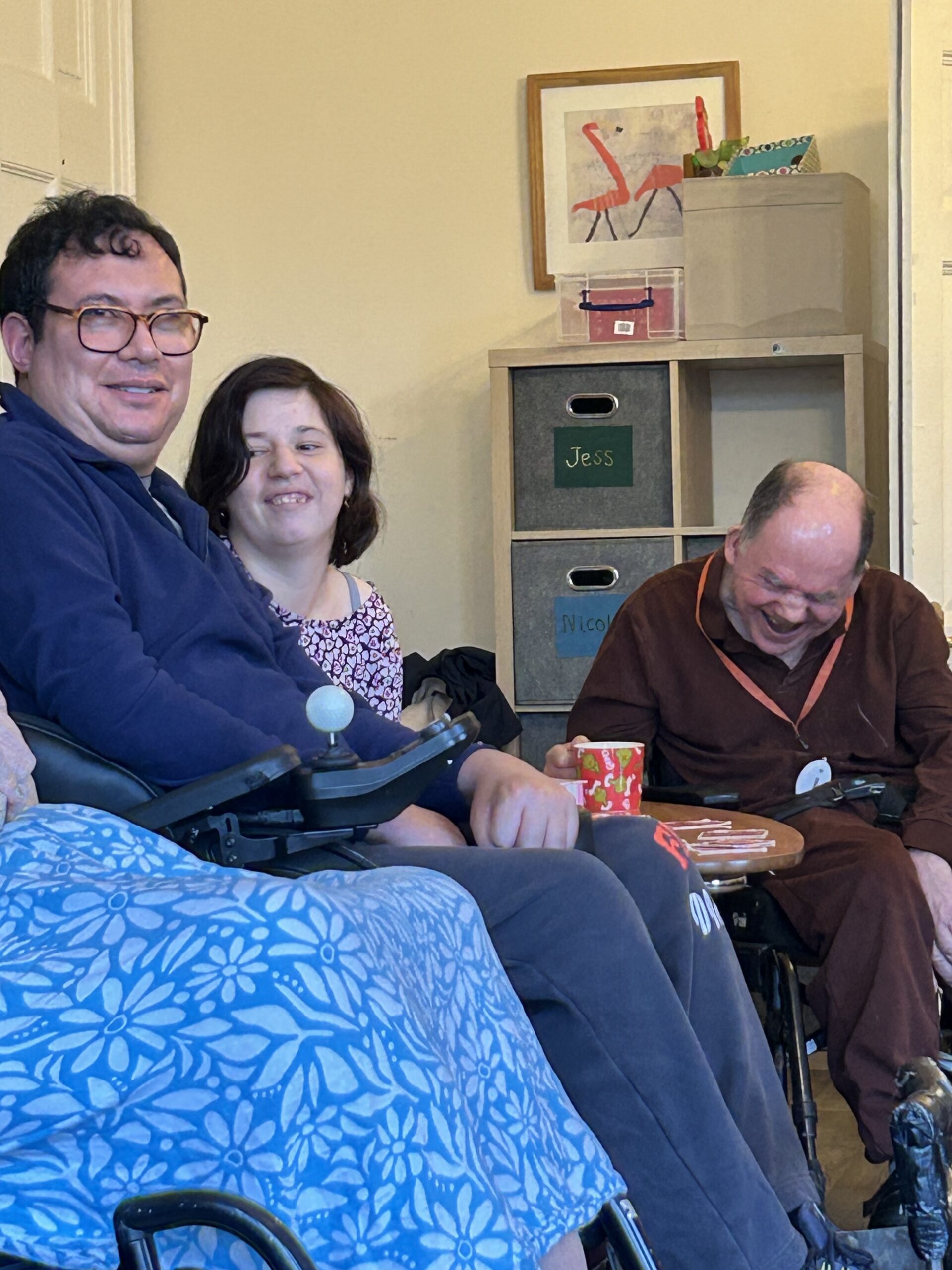 A man in a wheelchair laughs while a young man and woman, also in wheelchairs smile.